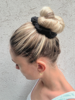 Una mujer con un peinado recogido adornado con un scrunchie negro en la parte superior de la cabeza.