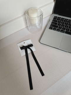 Prensita Moño negra sobre fondo claro, junto a una vela y una laptop.