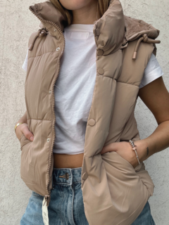 Chaleco estilo puffer con cuello alto y capucha desmontable. Cierre frontal con cremallera y botones. Piel sintética en todo el interior.