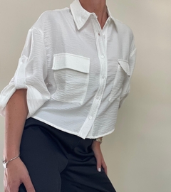 Camisa blanca de manga larga con dos bolsillos frontales, combinada con pantalones oscuros.