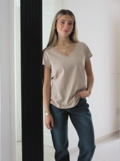 Mujer posando junto a un espejo, vistiendo una remera de color beige y jeans oscuros.