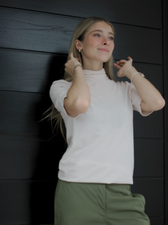 Modelo luciendo una polera ámbar de color claro con cuello, combinada con pantalones verdes, en un fondo negro.