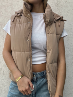 Chaleco estilo puffer con cuello alto y capucha desmontable. Cierre frontal con cremallera y botones. Piel sintética en todo el interior.