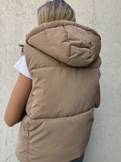 Chaleco estilo puffer con cuello alto y capucha desmontable. Cierre frontal con cremallera y botones. Piel sintética en todo el interior.