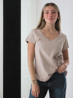 Mujer posando con una remera color beige y jeans, sonriendo frente a un espejo.