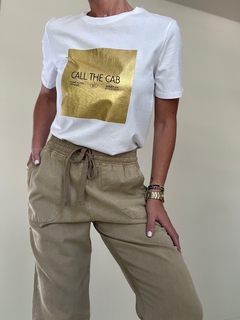 Pantalón Serena de color beige con una blusa blanca que tiene un diseño dorado.
