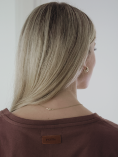 Mujer de espaldas con camiseta marrón y etiqueta de "INEDITA" en el cuello.
