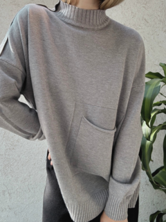 Sweater gris largo. Cuello alto y bolsillo frontal. Detalle de línea en los hombros y puños con frunce.