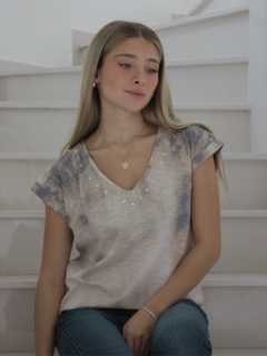 Modelo luciendo una remera Tierra de color beige con detalles en el escote, sentada en una escalera.