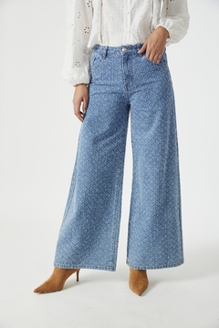 Jean Pirita de tiro alto en denim azul, con un diseño amplio y moderno, combinado con una blusa blanca y zapatos de tacón marrones.