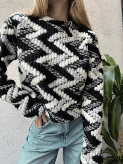 Modelo luciendo un sweater de borlas en tonos blanco y negro, con un diseño geométrico, combinado con jeans claros.