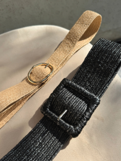 Dos cintos de yute, uno en color natural con un anillo dorado y otro en color negro con hebilla, sobre una superficie clara.