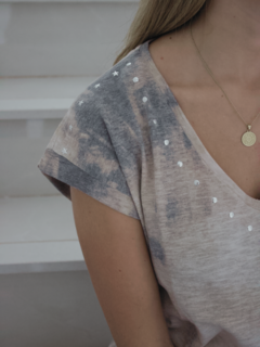 Remera Tierra de color gris claro con detalles en estrellas y lentejuelas, vista lateral de una mujer que la lleva puesta.