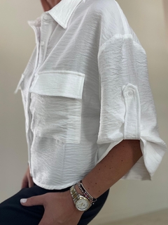 Camisa blanca de manga larga con dos bolsillos en el frente, detalle de textura arrugada y puños doblados.