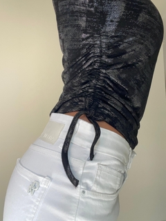 Remera Laurel de color negro con detalles de fruncido, vista lateral, combinada con pantalones blancos.