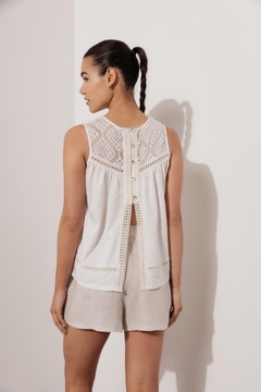 Vista trasera de una mujer luciendo una remera blanca con detalles de encaje y botones, combinada con pantalones cortos claros.