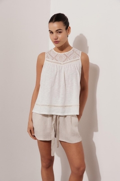 Remera blanca de mujer con detalles de encaje en el escote, combinada con shorts claros.
