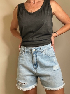 Mujer usando una remera negra con estrellas y bermudas de jean desgastadas, mostrando un estilo casual y moderno.