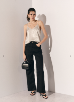 Modelo luciendo una blusa Venezia de tirantes finos en color plateado, combinada con pantalones negros y sandalias, sosteniendo un bolso negro.