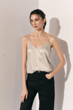 Blusa Venezia en color plateado, con tirantes finos, combinada con pantalones negros. Modelo posando con una expresión relajada.