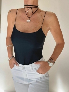 Una mujer viste un body negro de tirantes finos, con pantalones blancos y accesorios en la muñeca y el cuello.