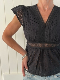 Blusa negra de mujer con detalles bordados y mangas cortas, combinada con pantalones de mezclilla.