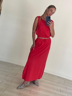Mujer posando con una pollera larga de lino roja, combinada con un top sin mangas y zapatos de diseño a rayas.