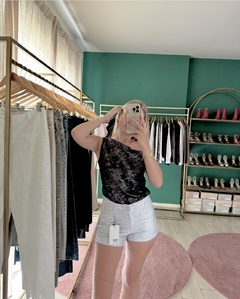 Una mujer posa frente a un espejo usando una remera de terciopelo negra y pantalones cortos blancos, en una tienda de ropa.