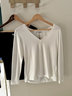 Remera EMILY de color blanco con mangas largas y escote en V, colgada en una percha.