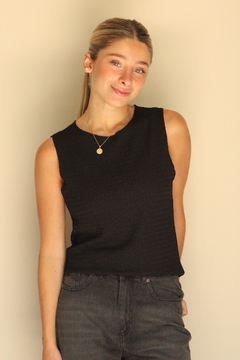 Modelo luciendo una remera sin mangas color negro, combinada con jeans oscuros, sonriendo frente a un fondo claro.