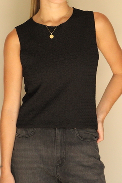 Remera sin mangas de color negro con textura, combinada con jeans oscuros y collar dorado.