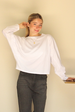 Modelo usando una remera blanca de manga larga con un diseño relajado, combinada con pantalones oscuros.