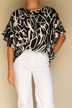 Blusa abstracta de estampado en blanco y negro, con mangas amplias y un diseño moderno, combinada con pantalones blancos.
