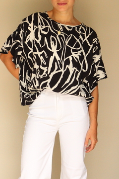 Modelo vistiendo una blusa abstracta de colores blanco y negro, combinada con pantalones blancos.