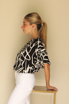Modelo usando una blusa abstracta en blanco y negro, de perfil, con cabello recogido y apoyada en una mesa.