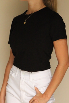 Remera corta negra de Zara, vista lateral, combinada con pantalones blancos.