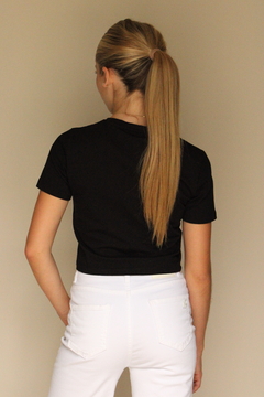 Modelo de espaldas vistiendo una remera corta negra de ZARA, combinada con pantalones blancos.