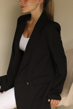 Mujer usando un saco de color negro, con un look elegante y moderno, posando en un entorno neutral.