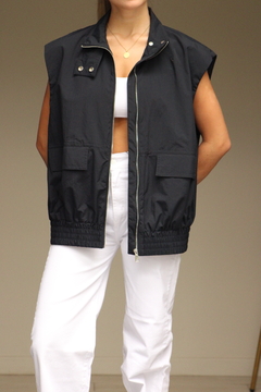 Chaleco Rompeviento negro sin mangas, con cierre frontal y bolsillos, combinado con pantalones blancos.