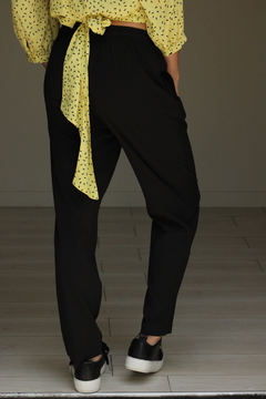 Pantalón Amalfi negro visto desde atrás, combinado con una blusa amarilla con estampado.