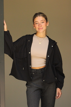 Modelo con rompeviento negro sobre una camiseta beige y jeans oscuros, sonriendo y apoyada en una pared.