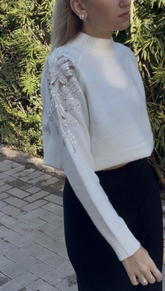 Sweater largo con diseño de strass en los hombros que caen por la manga. Cuello alto. Color crudo