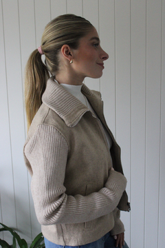 Campera Marea de color beige, con cierre frontal y mangas de punto, combinada con una camiseta blanca y jeans, exhibida en un entorno minimalista.
