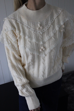 Sweater Mar tejido color crema con detalles de trenzas y encajes, decorado con pompones pequeños y cuello alto acanalado