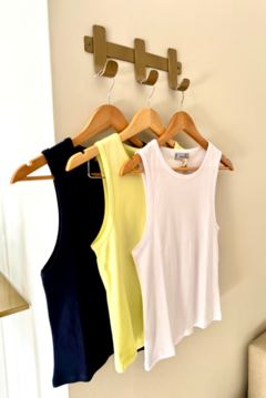 Tres musculosas colgadas en percheros: una negra, una amarilla y una blanca.