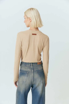 Remera Laurel de color beige, con un diseño de manga larga y textura acanalada, vista trasera de una mujer con cabello corto.