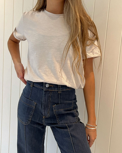 Remera ZOE de color blanco, combinada con jeans oscuros, modelo femenino mostrando la parte superior de la prenda.