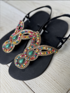Sandalias multicolor con detalles brillantes y piedras en tonos verdes, en fondo negro.