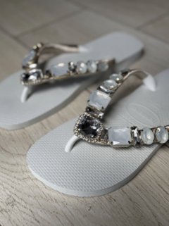 Hawaianas blancas con detalles de piedras brillantes en la tira, sobre un fondo de piso claro.