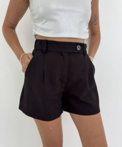 Shorts negros con cintura alta y botón, combinados con una blusa plateada, presentados en un fondo blanco.